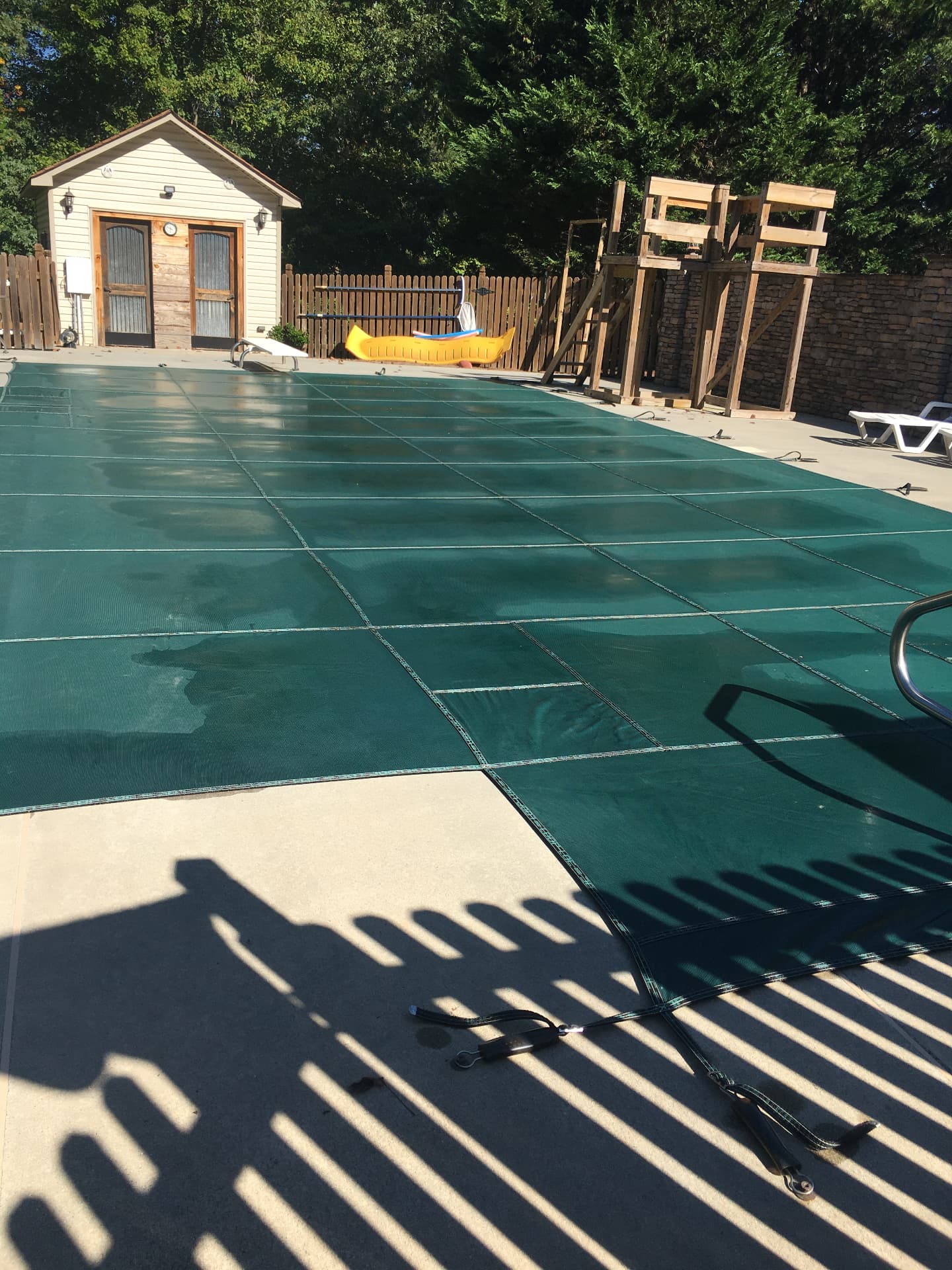 Green anchored pool cover beside a pool house and wooden fence