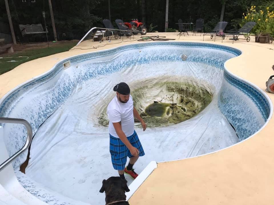 A crew member walking through a drained pool with a torn, sagging vinyl liner ready to come out