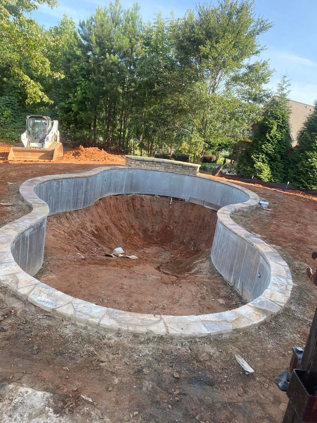 Curved pool walls with flagstone coping and a stacked-stone feature wall taking shape