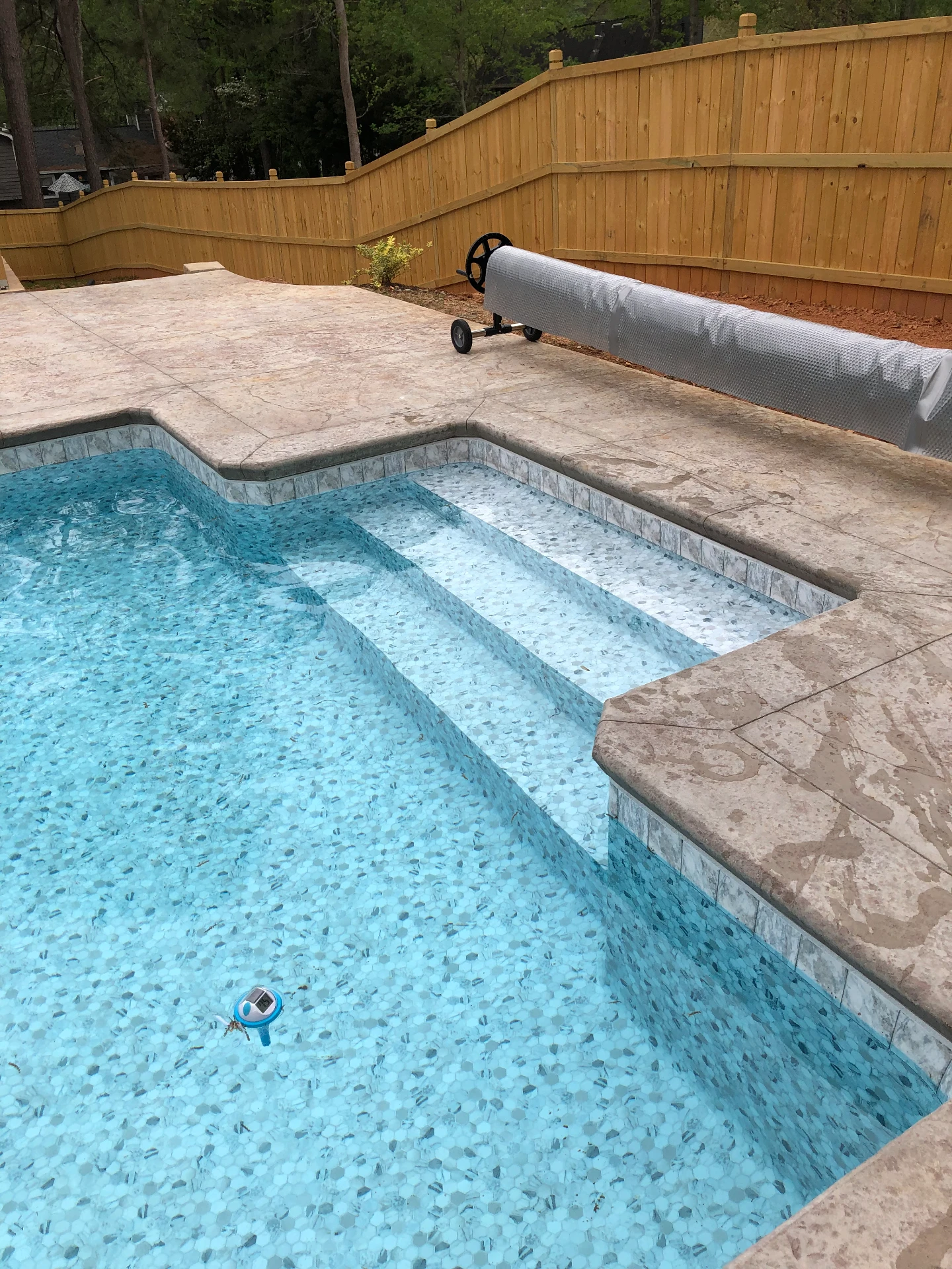 Blue patterned vinyl liner and wide entry steps beside a pool cover reel